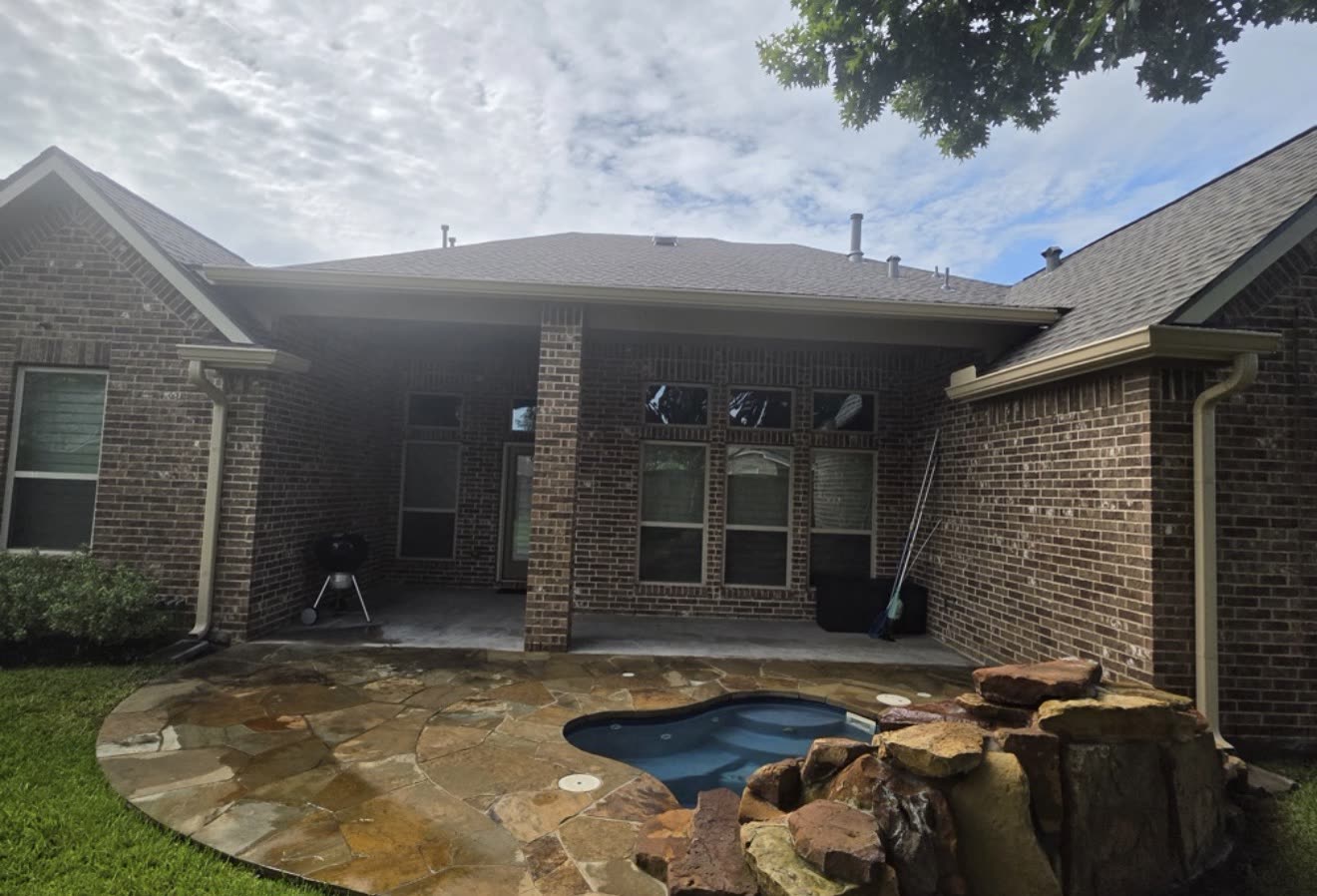 Back of a brick home with seamless gutters above a patio