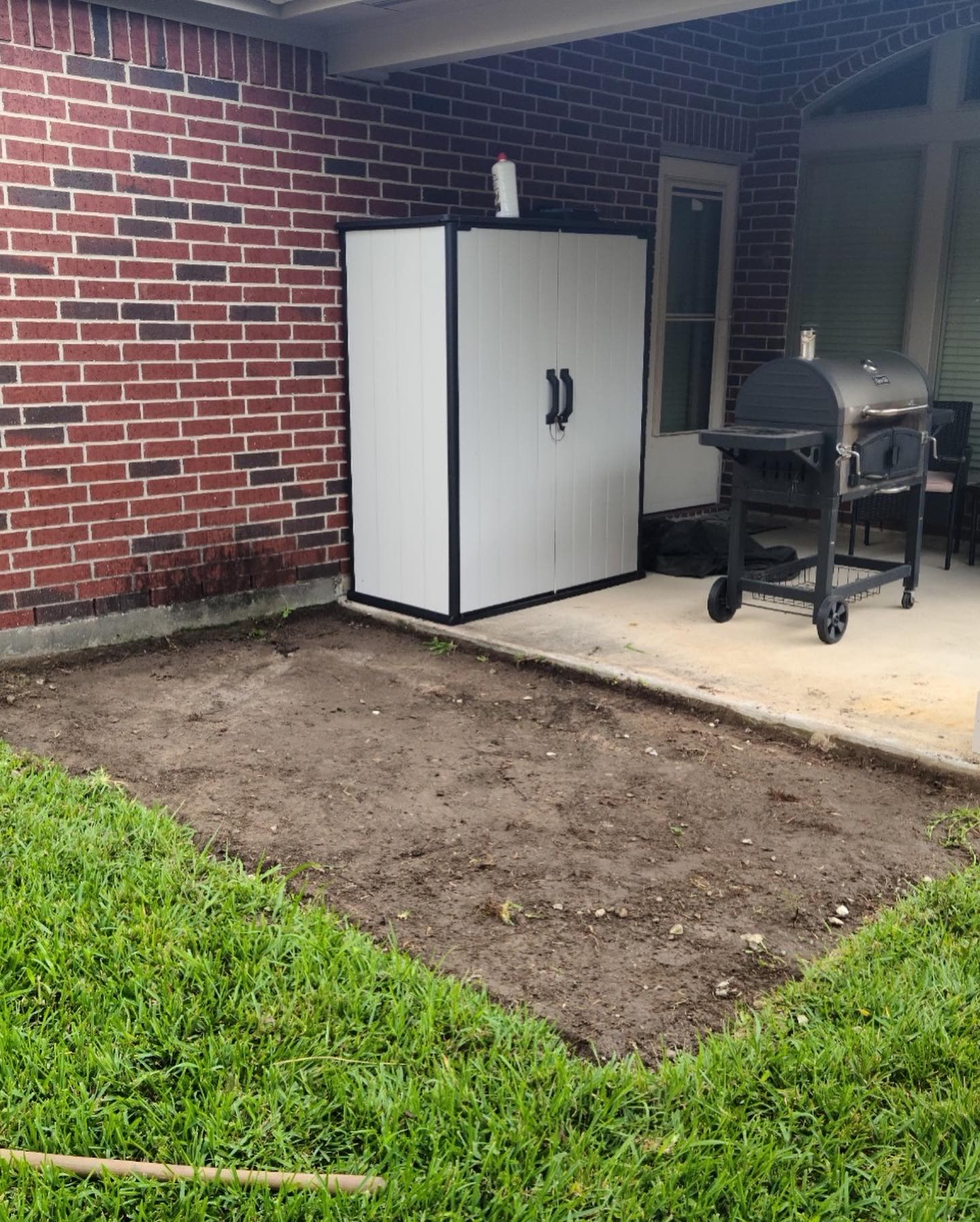 Graded dirt area prepared for a new concrete pad beside a patio