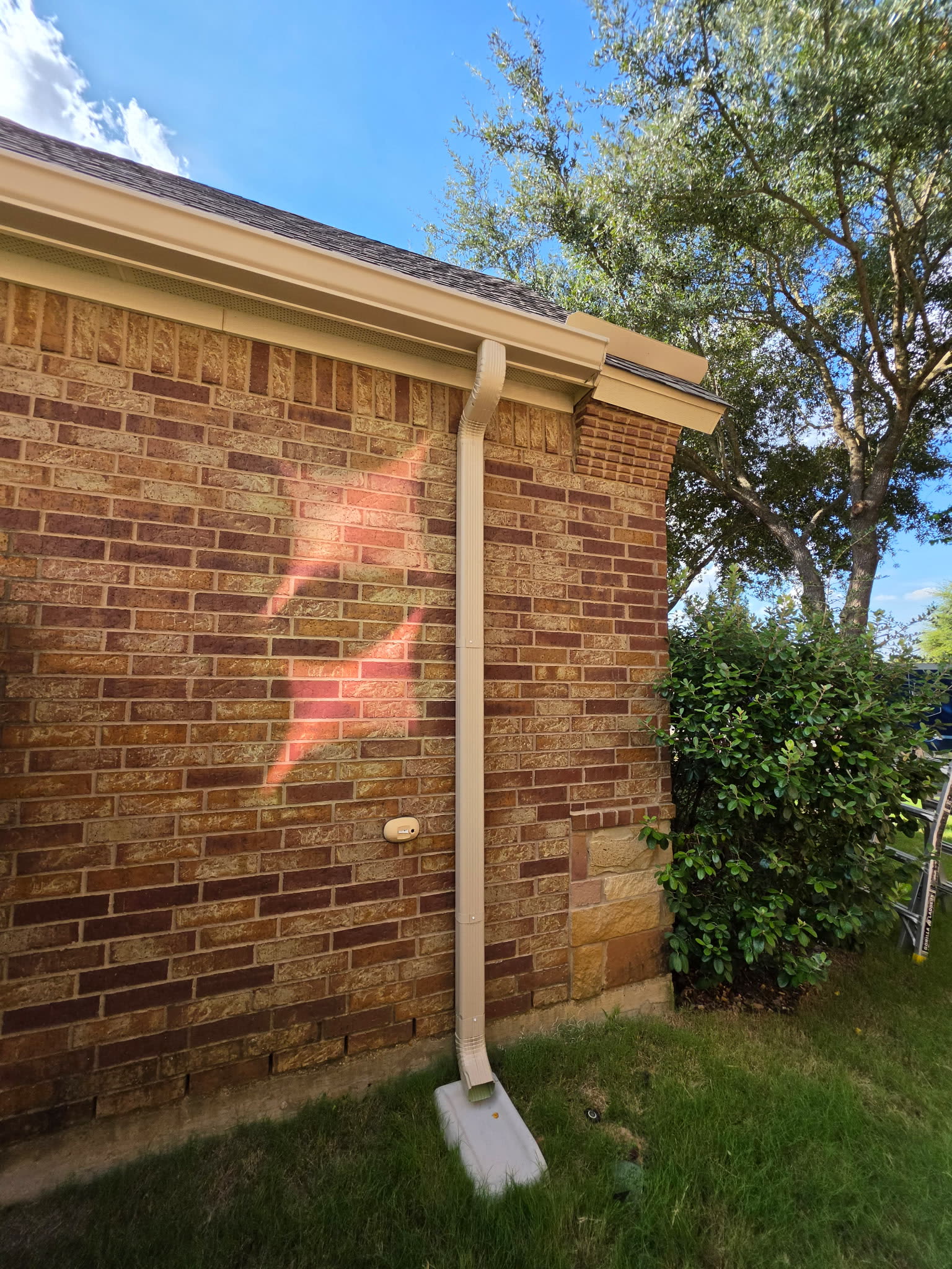 Tan seamless gutter and downspout at the corner of a brick home