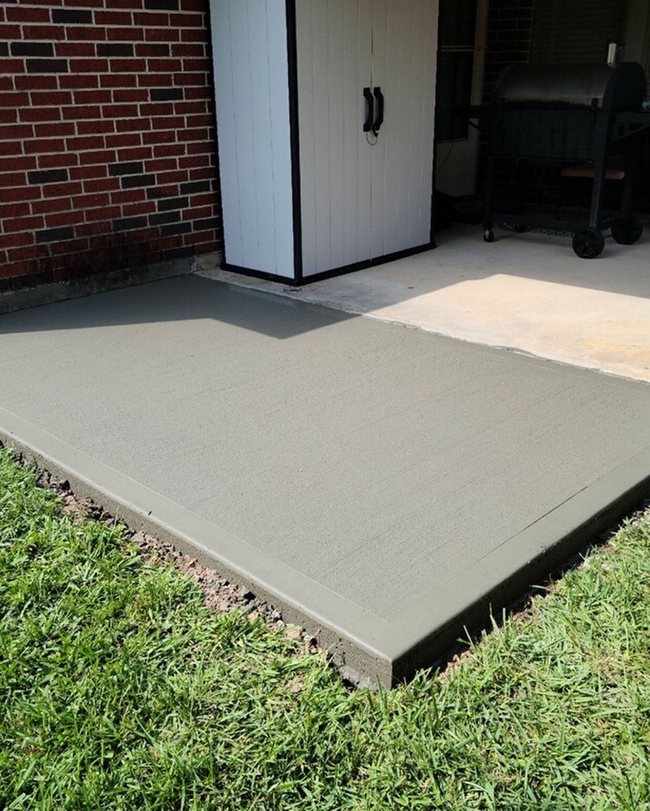 New concrete pad poured next to a brick home's back patio