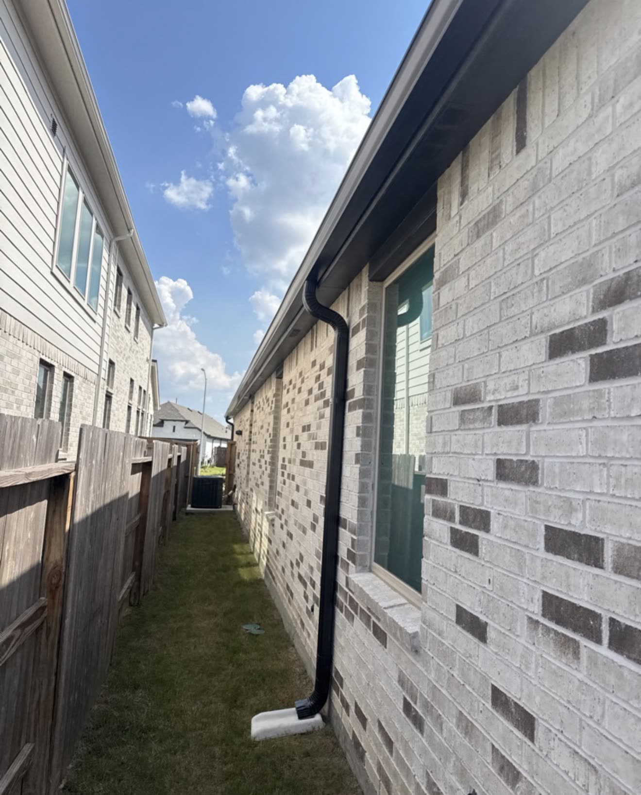 Dark bronze seamless gutter and downspout along a light brick home