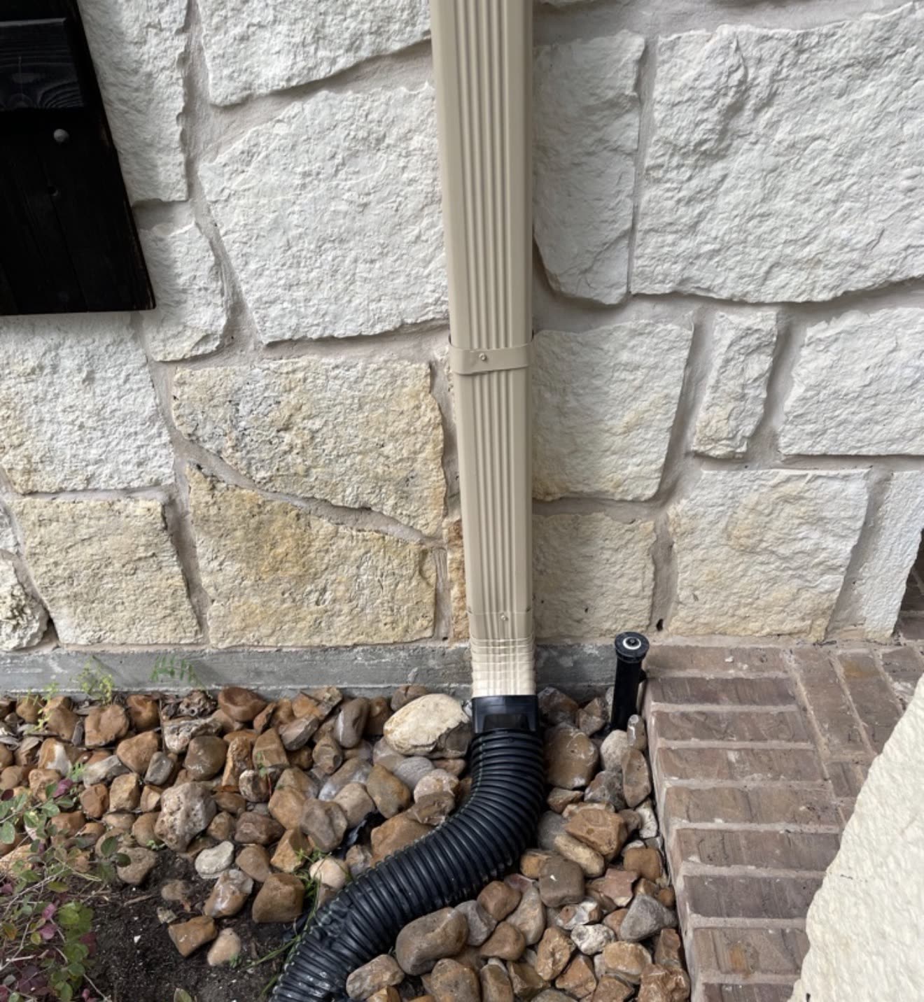 Downspout connected to an underground drain pipe beside a stone wall